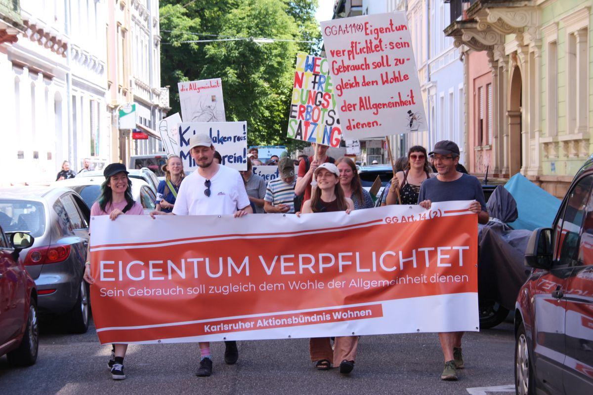 Demonstranten tragen ein Transparent mit der Aufschrift "Eigentum verpflichtet!" Dahinter sieht man weitere Demonstranten mit weiteren Transparenten.